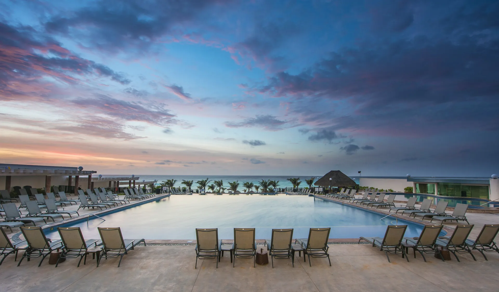 Pool deck with lounge chairs facing the ocean at Seadust Cancún Family Resort.
