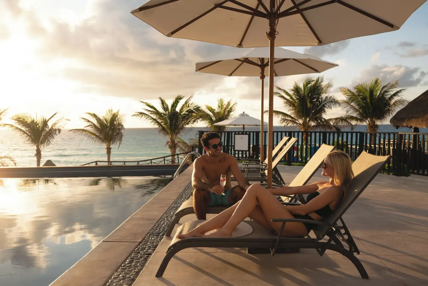 Poolside loungers and umbrellas by the ocean at Seadust Cancún Family Resort.