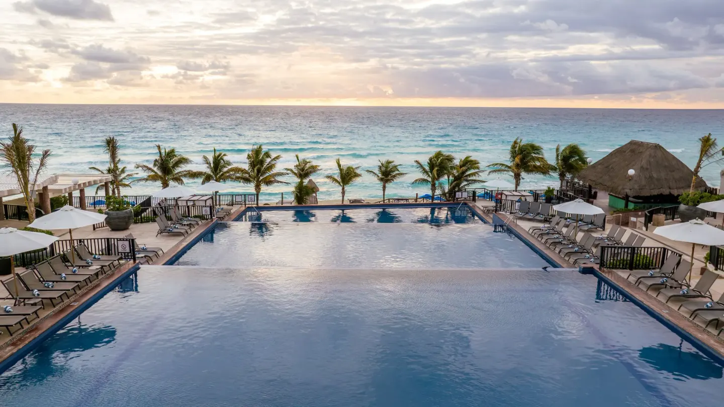 Oceanfront pool with loungers and palms at Seadust Cancún Family Resort.