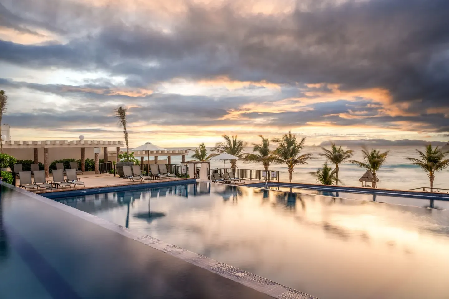 Infinity-style pool with ocean and sunset clouds at Seadust Cancún Family Resort.
