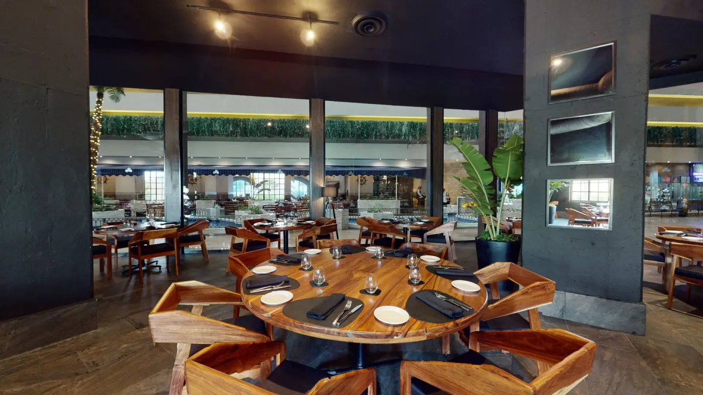 Dark-toned restaurant dining room with round wooden tables at Seadust Cancún Family Resort.