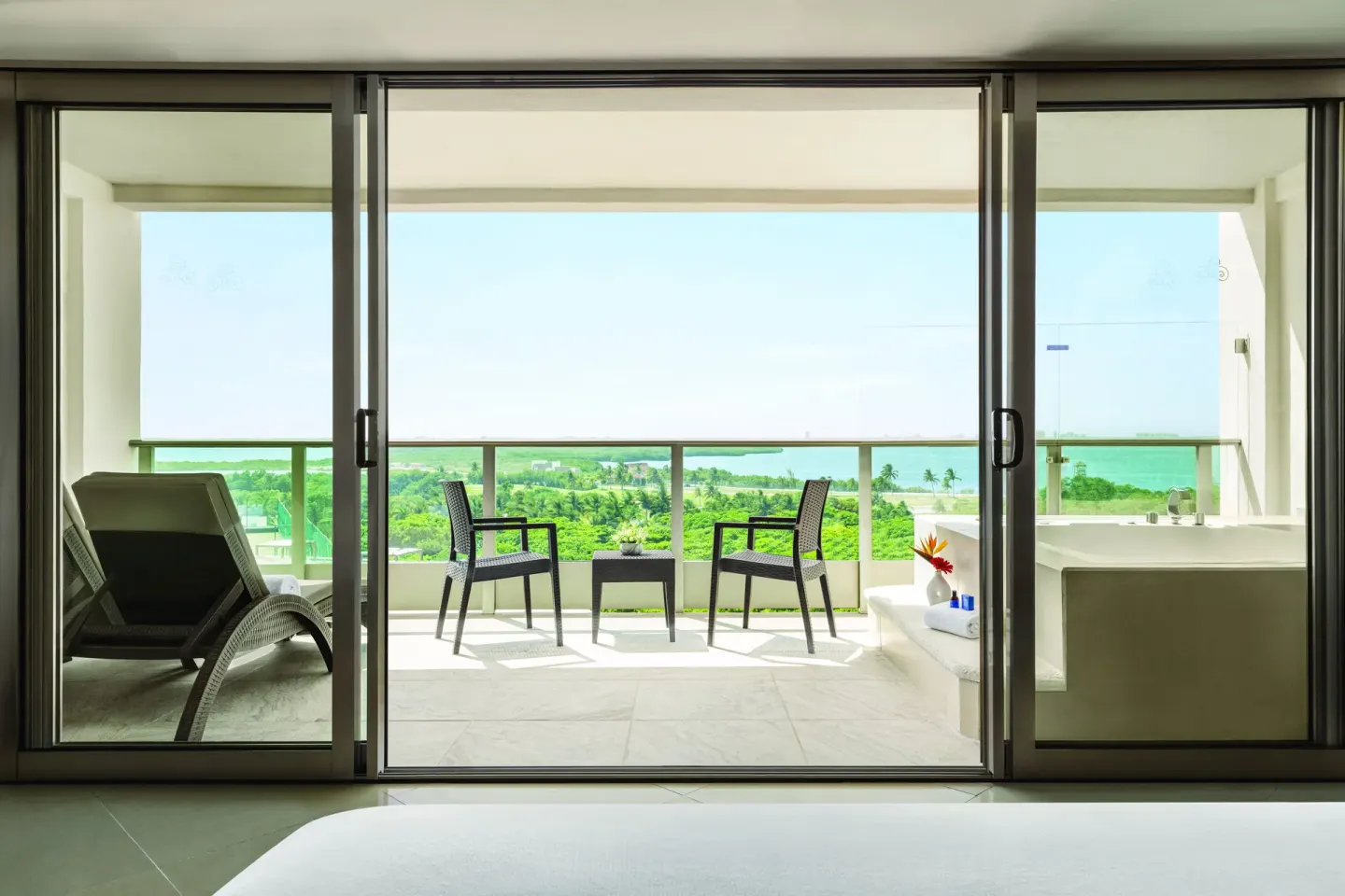 Deluxe Suite balcony with chairs, lounge chair, and tub at Seadust Cancún Family Resort.