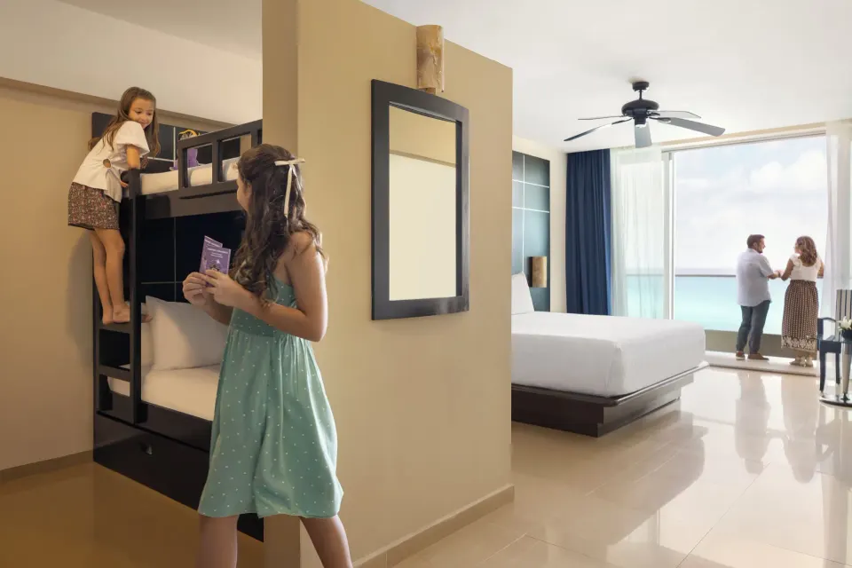 Family Suite with children by bunk beds and adults on the balcony at Seadust Cancún Family Resort.