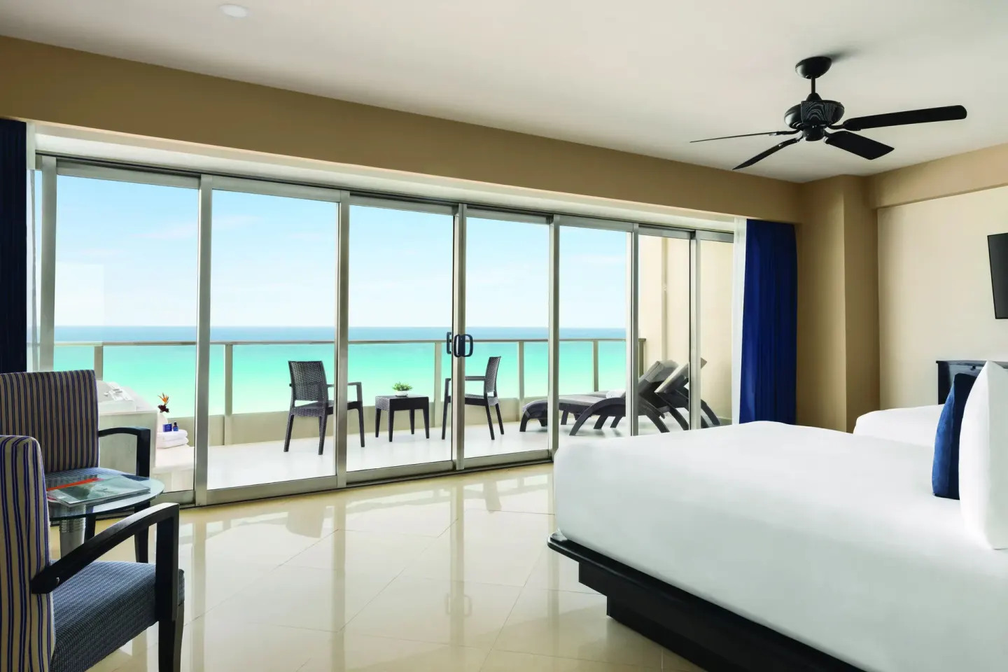 Oceanfront Suite bedroom with balcony seating at Seadust Cancún Family Resort overlooking the sea.