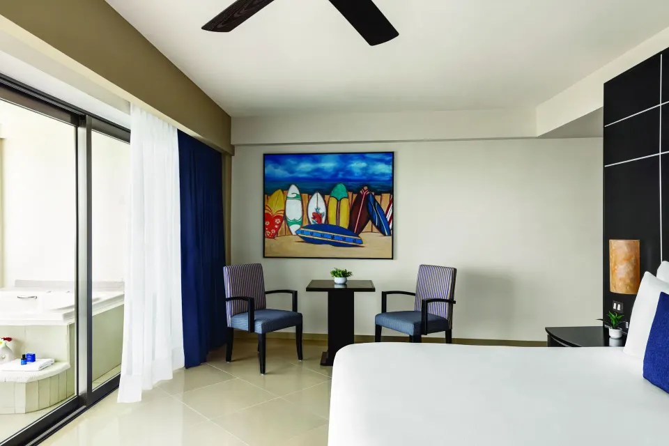 Oceanfront Suite king bed and sitting area at Seadust Cancún Family Resort near balcony doors.