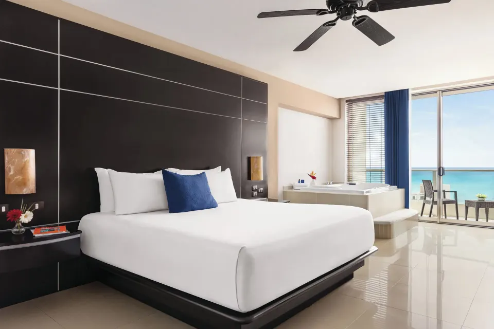 Premium Suite king bed with blue accent pillow and ocean-facing balcony at Seadust Cancún Family Resort.