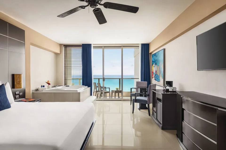 Premium Suite with king bed, TV, sitting area, tub and ocean-facing balcony at Seadust Cancún Family Resort.