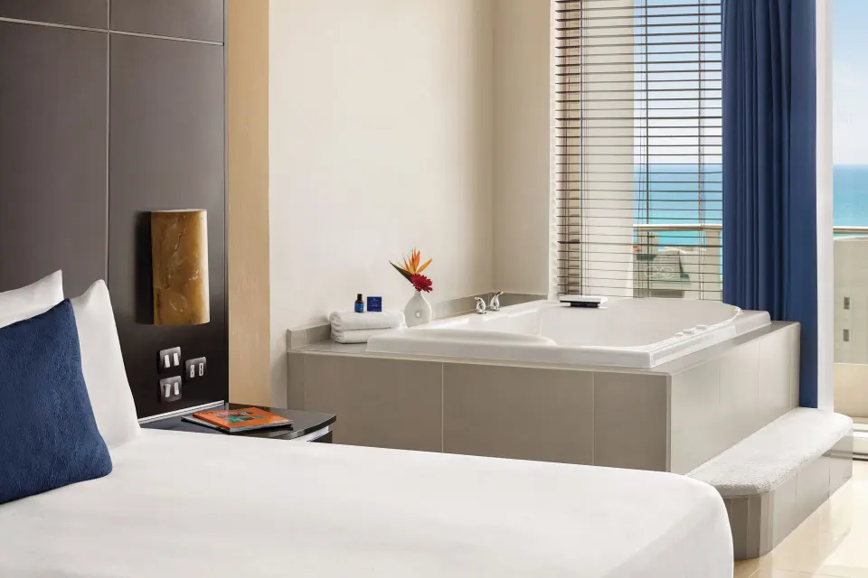 Premium Suite soaking tub beside the king bed and ocean-facing window at Seadust Cancún Family Resort.