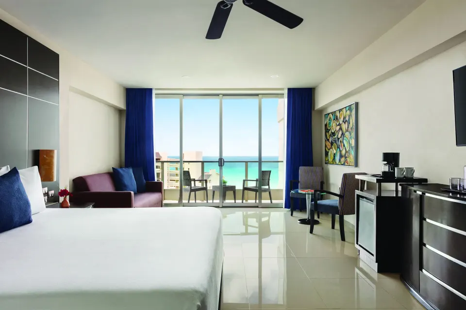 Standard Suite king bed, sofa, and balcony view at Seadust Cancún Family Resort.