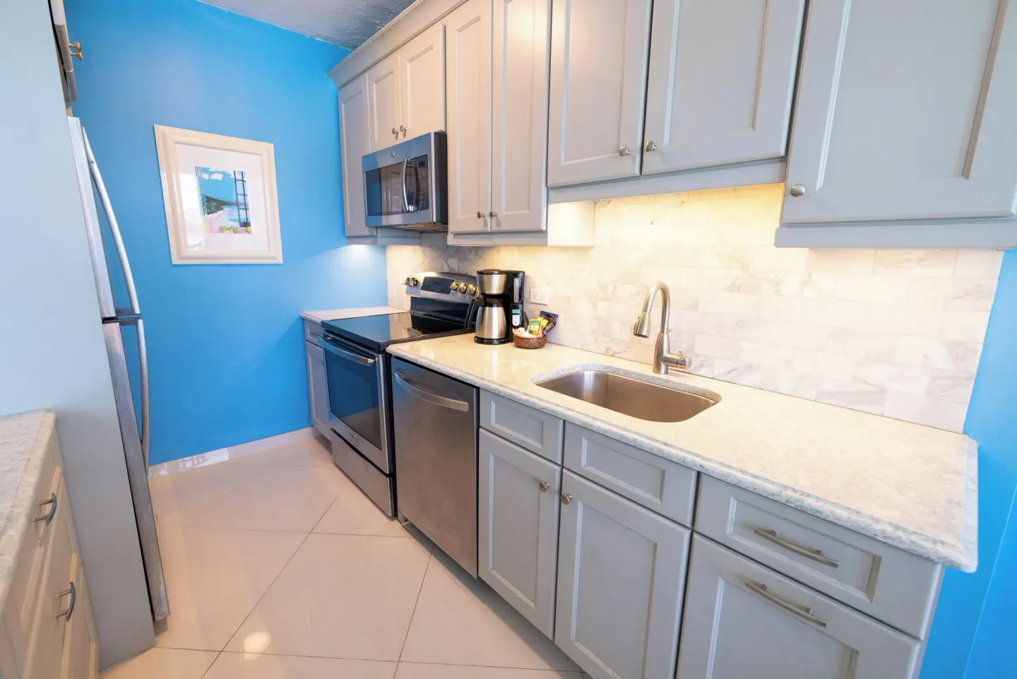 Compact suite kitchen at Secret Harbour Beach Resort with blue walls and gray cabinetry.