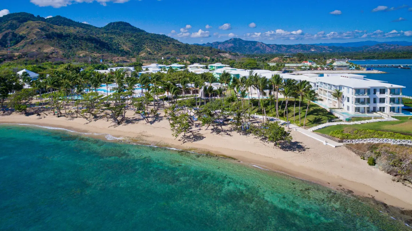 Aerial view of Senator Puerto Plata along the beach with mountains behind the resort.