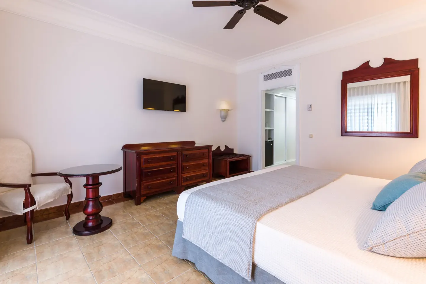 Guest room with a bed, dresser, wall TV, mirror, and sitting area at Senator Puerto Plata.