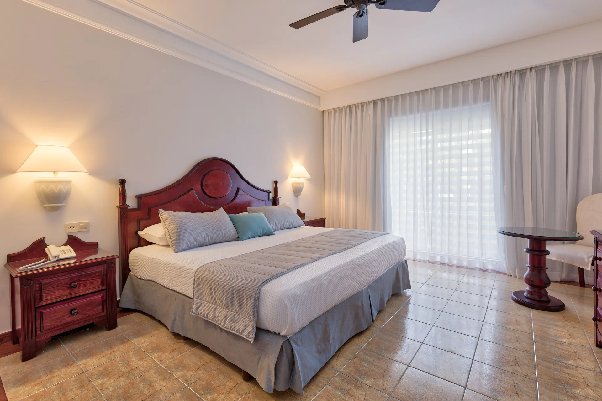 Guest room with a king bed, nightstands, glass-top table, and large curtains at Senator Puerto Plata.