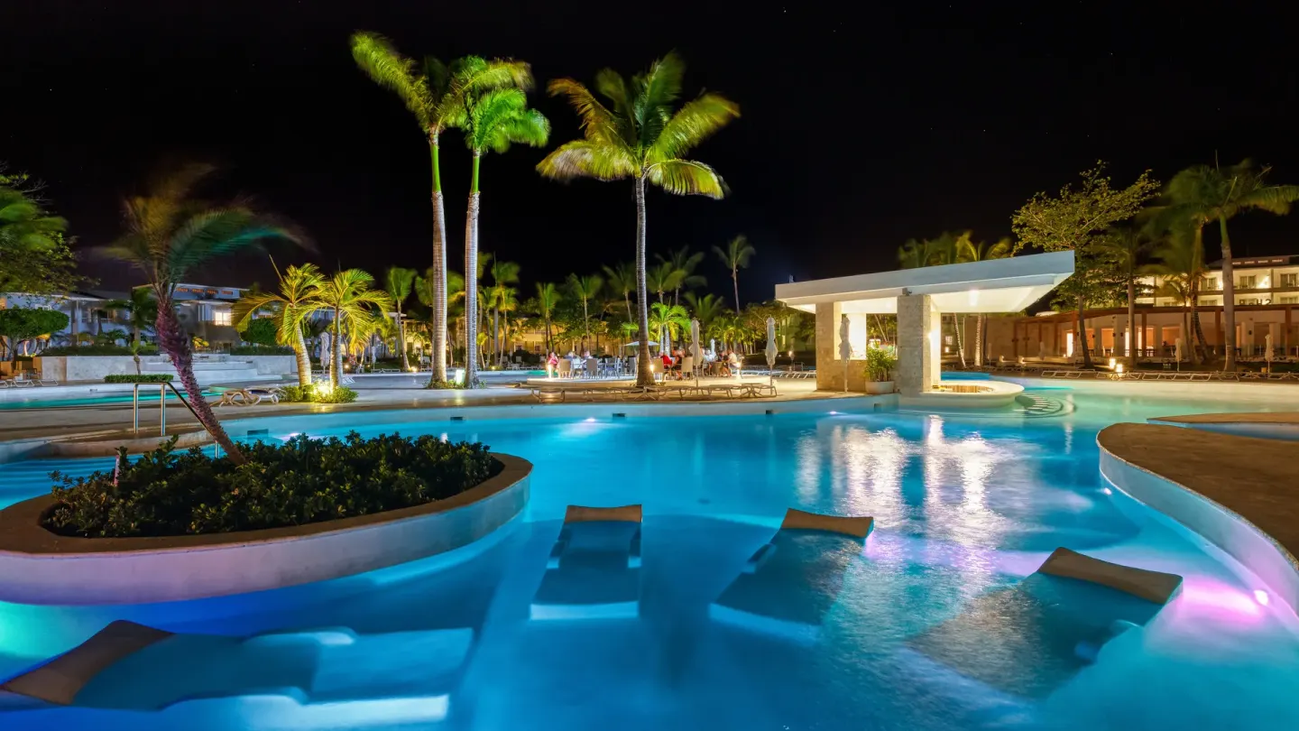 Nighttime pool at Senator Puerto Plata with glowing water, palms, and submerged loungers.
