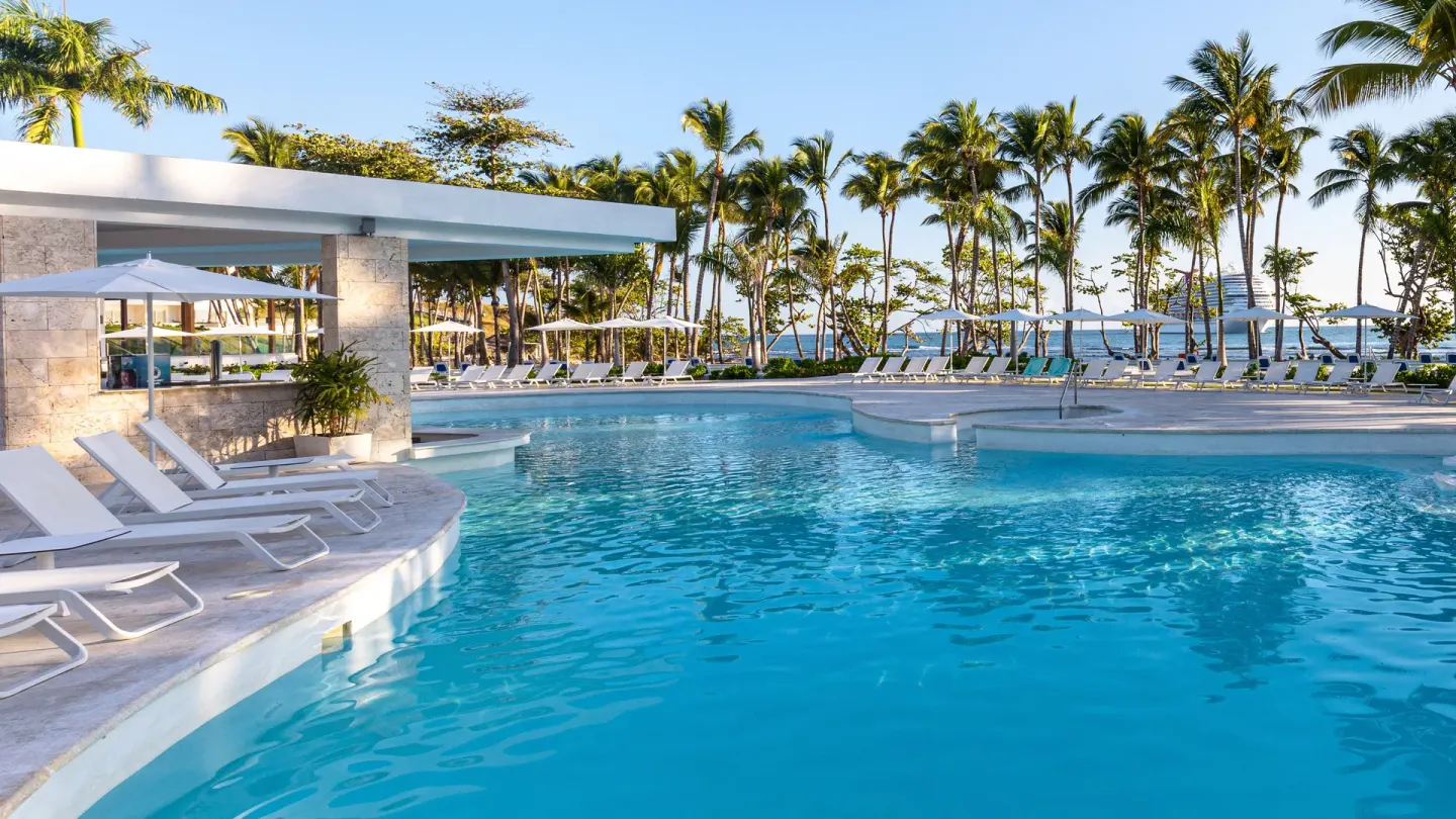 Large pool with loungers, umbrellas, palms, and ocean views at Senator Puerto Plata.