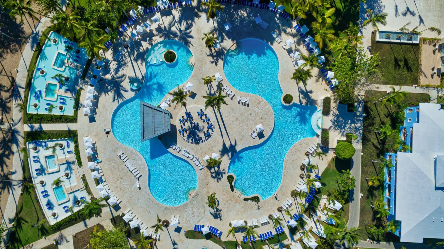Overhead pool complex at Senator Puerto Plata with curved pools, loungers, and palm trees.