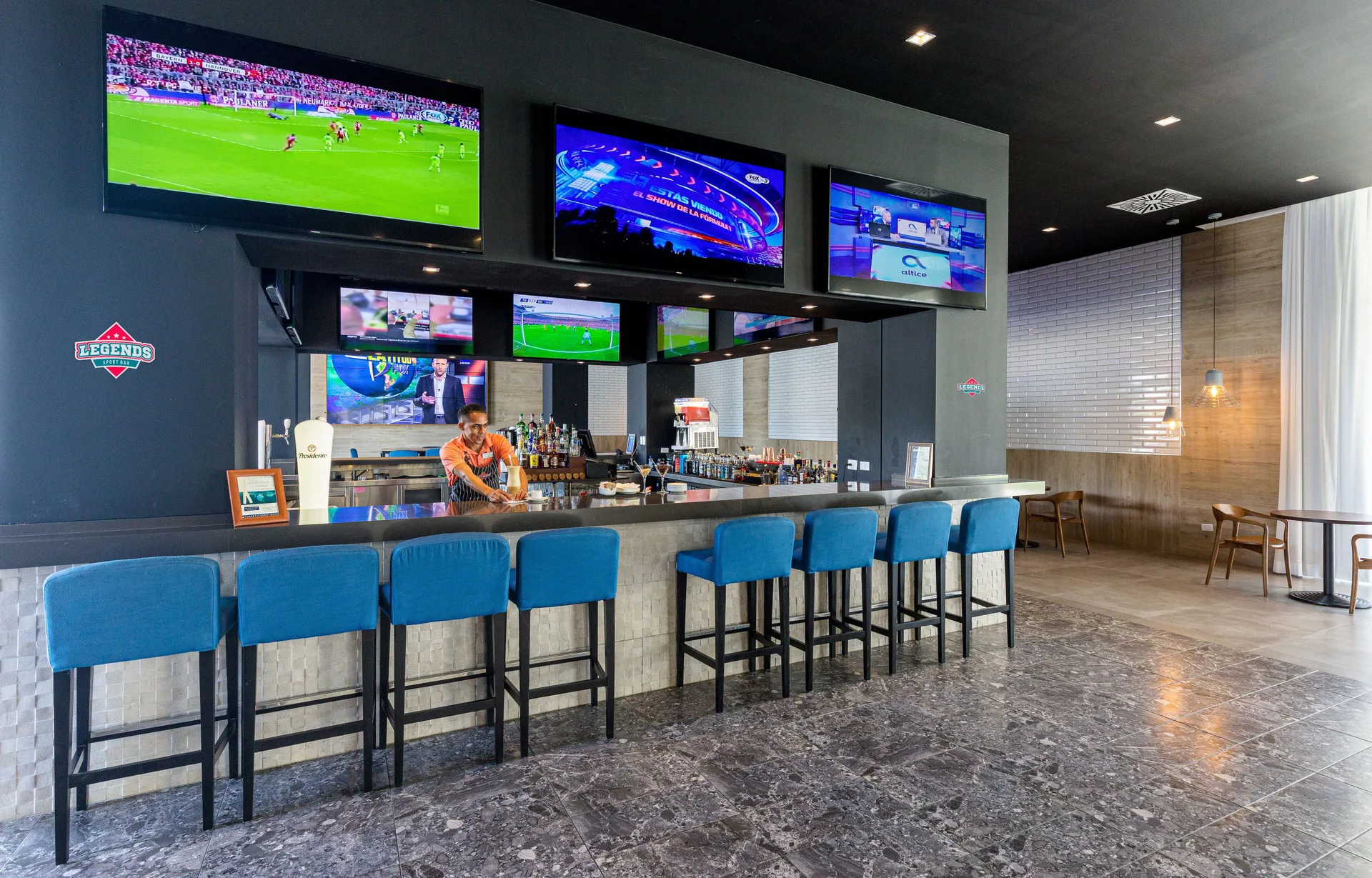 Legends sports bar at Senator Puerto Plata with blue stools, a counter, and multiple TVs.