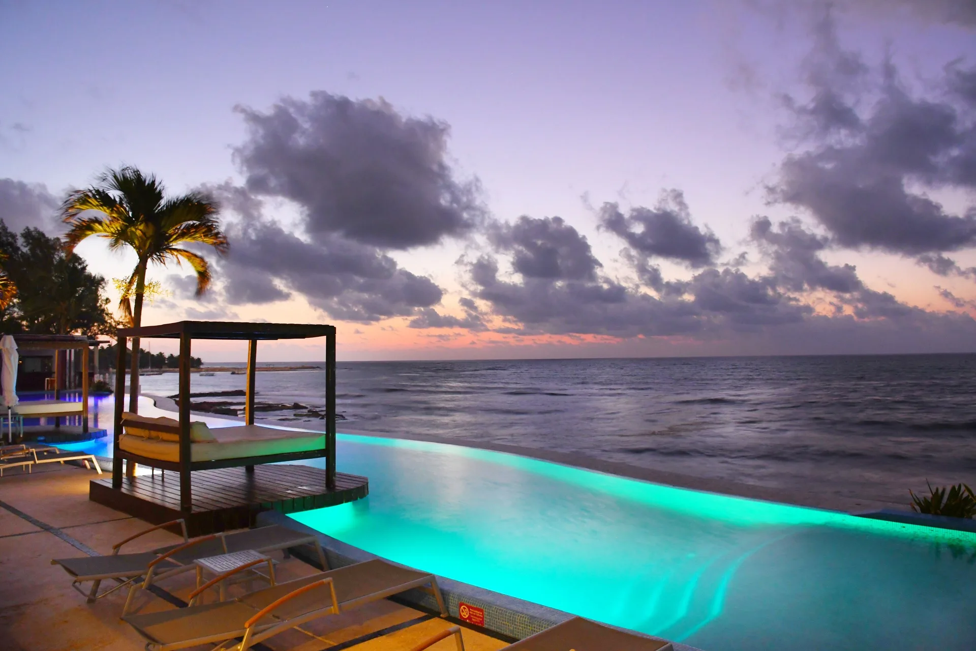 Illuminated infinity pool beside the ocean at dusk at Senses Riviera Maya Oceanfront.