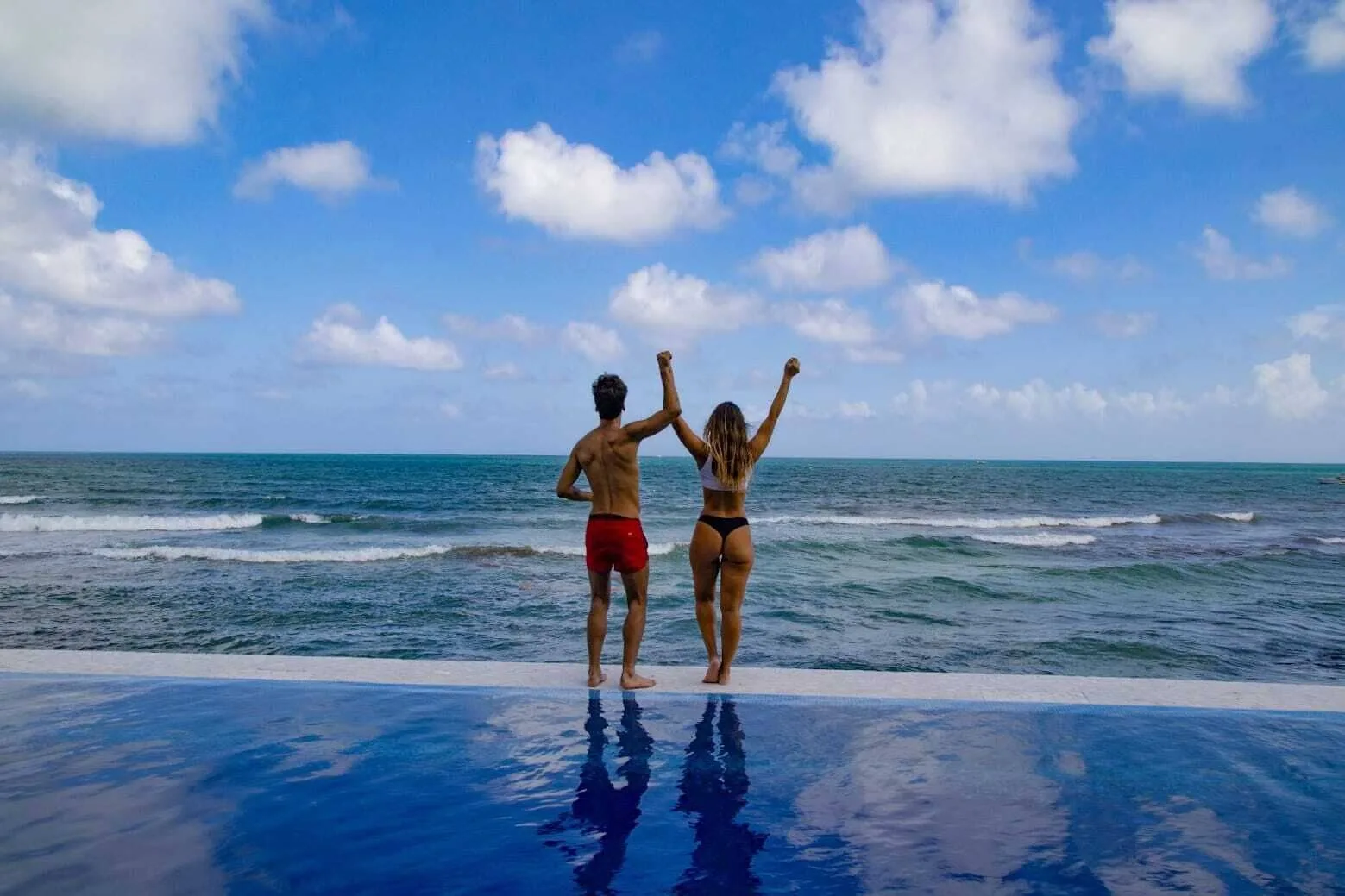 Two guests stand at the infinity pool edge facing the ocean at Senses Riviera Maya Oceanfront.