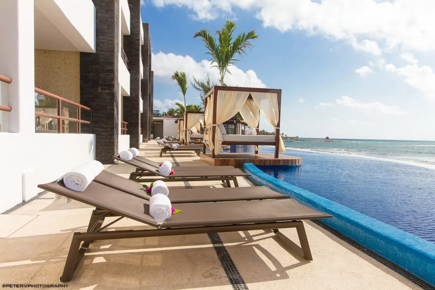 Poolside loungers and curtained daybeds face the ocean at Senses Riviera Maya Oceanfront.