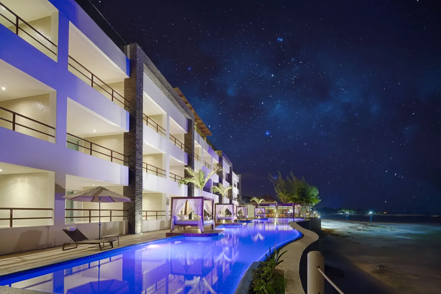 Resort building, glowing pool, and beach under a starry sky at Senses Riviera Maya Oceanfront.