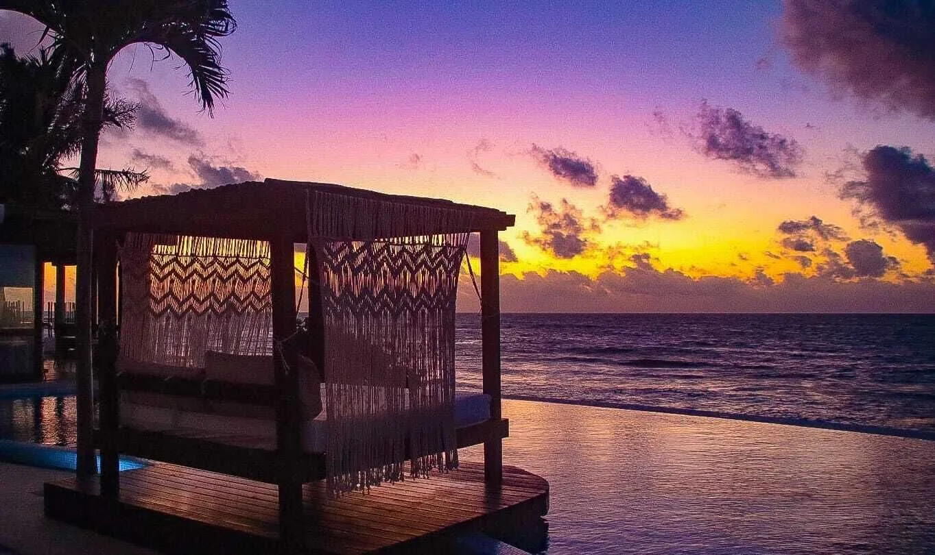 Canopied pool daybed silhouetted against a purple ocean sunset at Senses Riviera Maya Oceanfront.