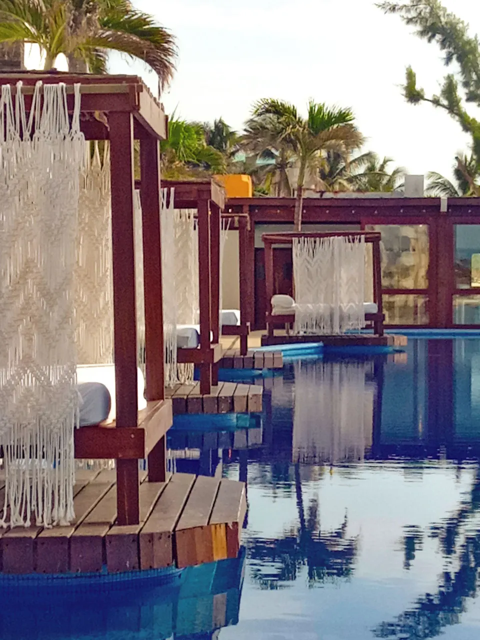 Wood-framed daybeds line the pool with palm trees at Senses Riviera Maya Oceanfront.