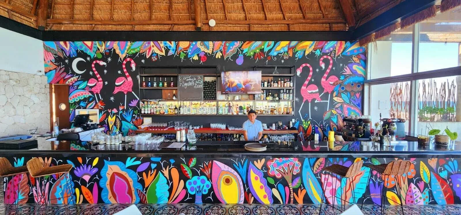 A colorful bar with flamingo murals and a bartender at Senses Riviera Maya Oceanfront.