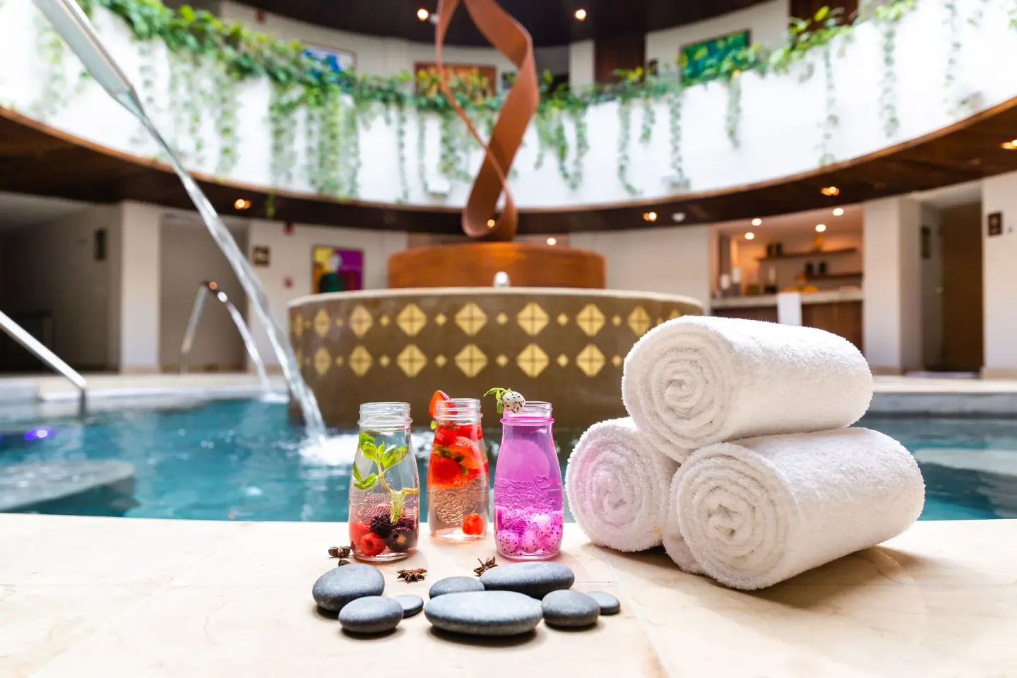 Rolled towels and infused drinks beside an indoor spa pool at Sensira Resort & Spa Riviera Maya.