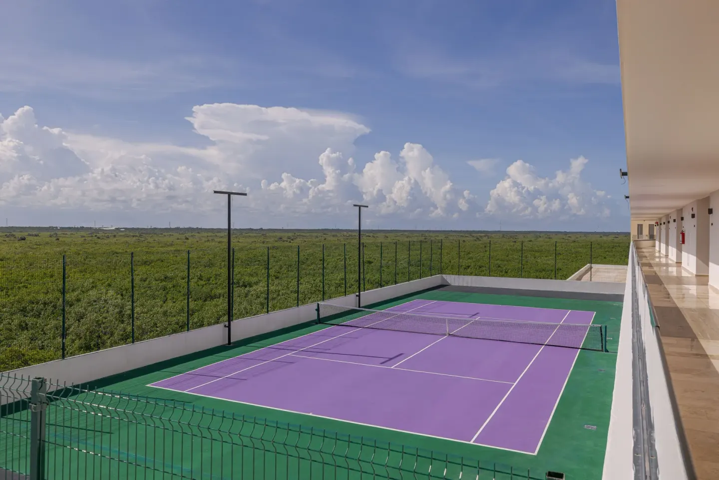Purple outdoor tennis court beside guest-room corridors at Sensira Resort & Spa Riviera Maya.