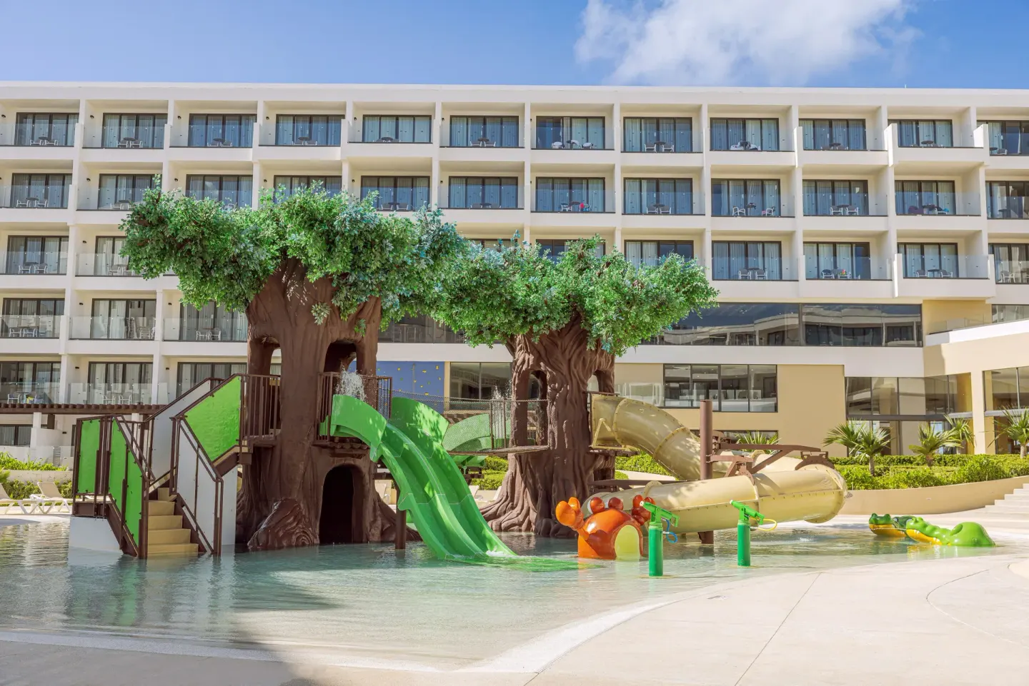 Tree-themed splash pool with slides in front of balconies at Sensira Resort & Spa Riviera Maya.