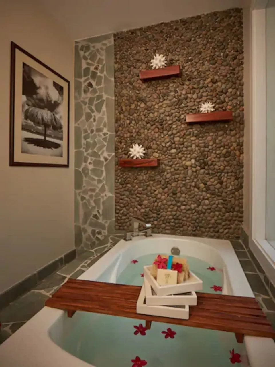 Soaking bathtub with pebble feature wall and floral accents at Serenity At Coconut Bay