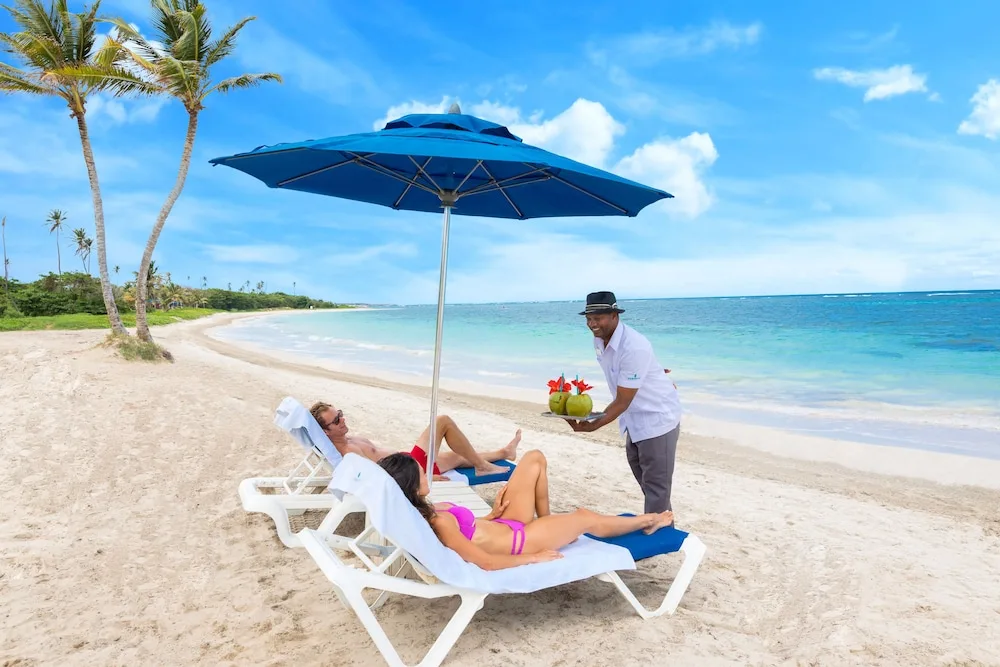 Guests lounging on beach chairs while server brings refreshments at Serenity At Coconut Bay