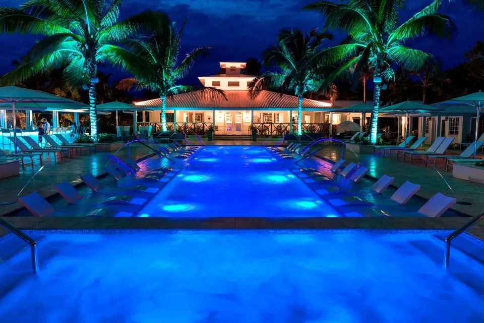 Resort pool lit in blue at night with loungers and palm trees at Serenity At Coconut Bay