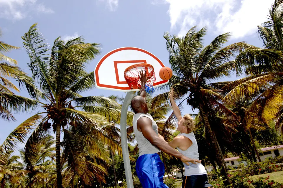 Guests playing basketball under palm trees on an outdoor court at Serenity At Coconut Bay.