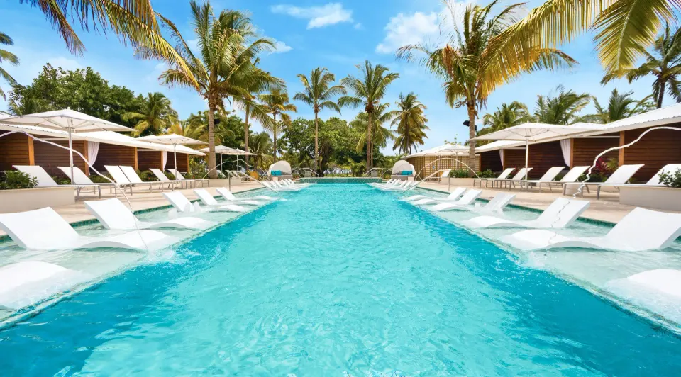 Long resort pool with in-pool loungers and cabanas at Serenity At Coconut Bay