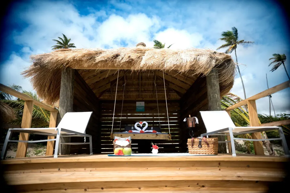 Thatched beachfront cabana with sun chairs and heart-shaped towel swans at Serenity At Coconut Bay