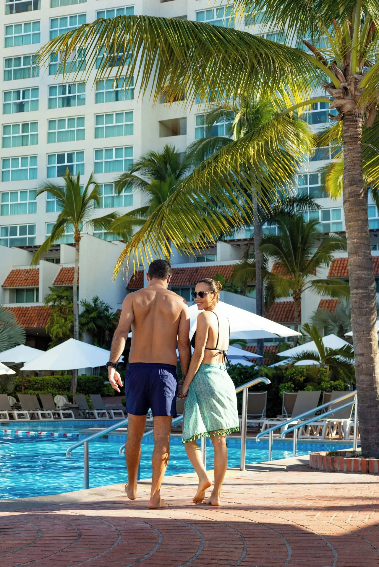 Couple walking beside the pool and palms at Sheraton Buganvilias Puerto Vallarta.