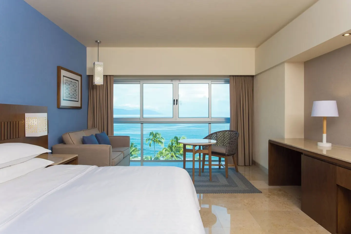 Ocean-view king guest room with sofa and table at Sheraton Buganvilias Puerto Vallarta.