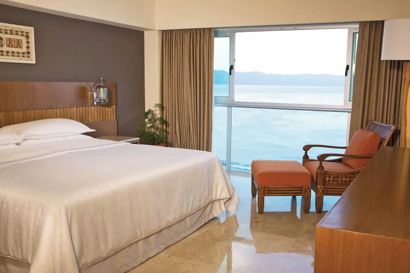 King guest room with ocean-facing window and lounge chair at Sheraton Buganvilias Puerto Vallarta.