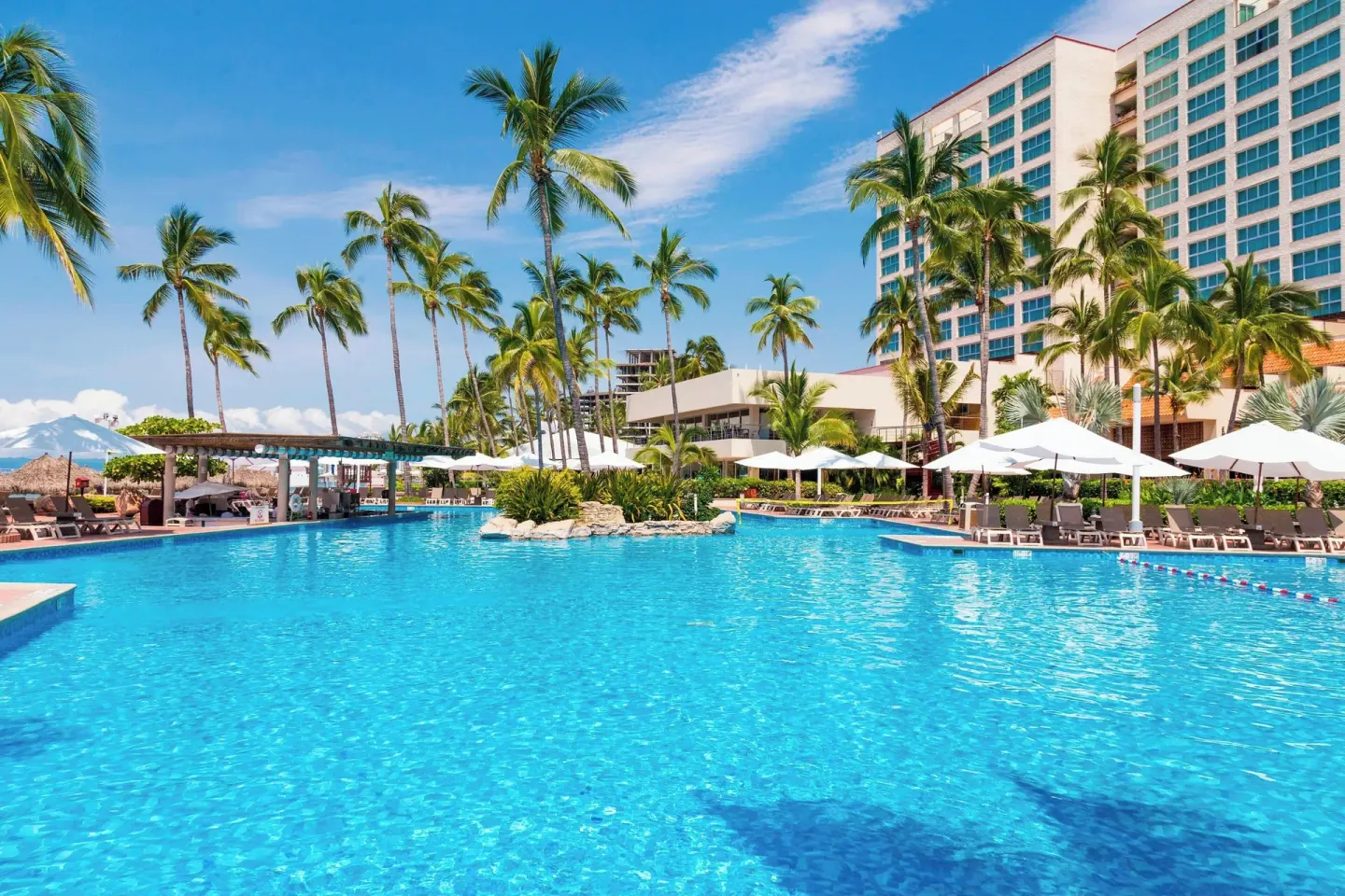 Resort pool with palms, umbrellas, and hotel tower at Sheraton Buganvilias Puerto Vallarta.