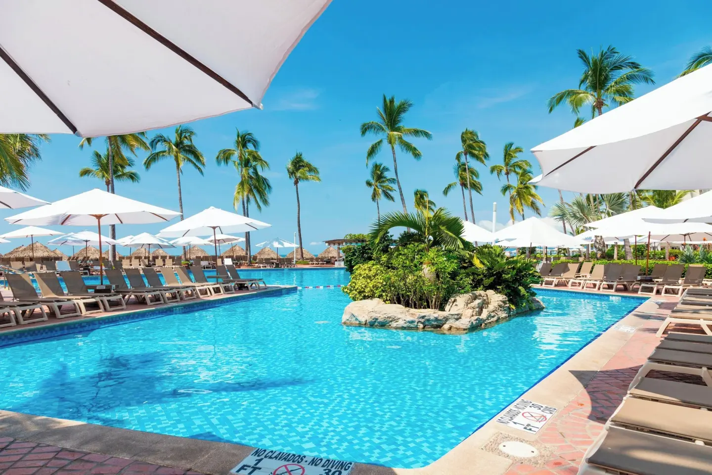 Resort pool with loungers, umbrellas, and palms at Sheraton Buganvilias Puerto Vallarta.