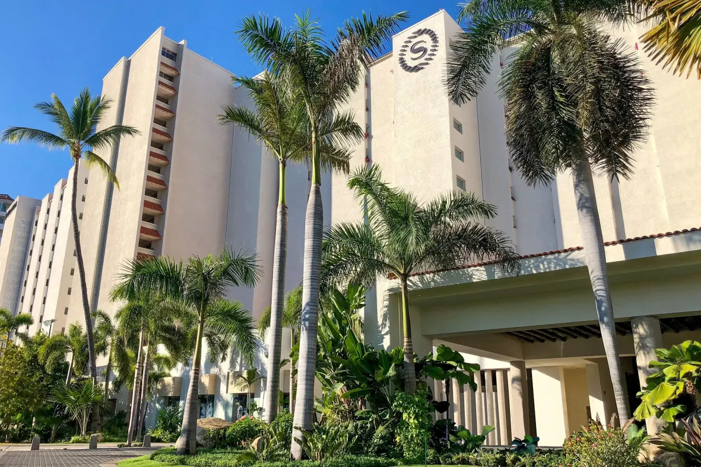 Resort tower exterior with palms and landscaped entry at Sheraton Buganvilias Puerto Vallarta.