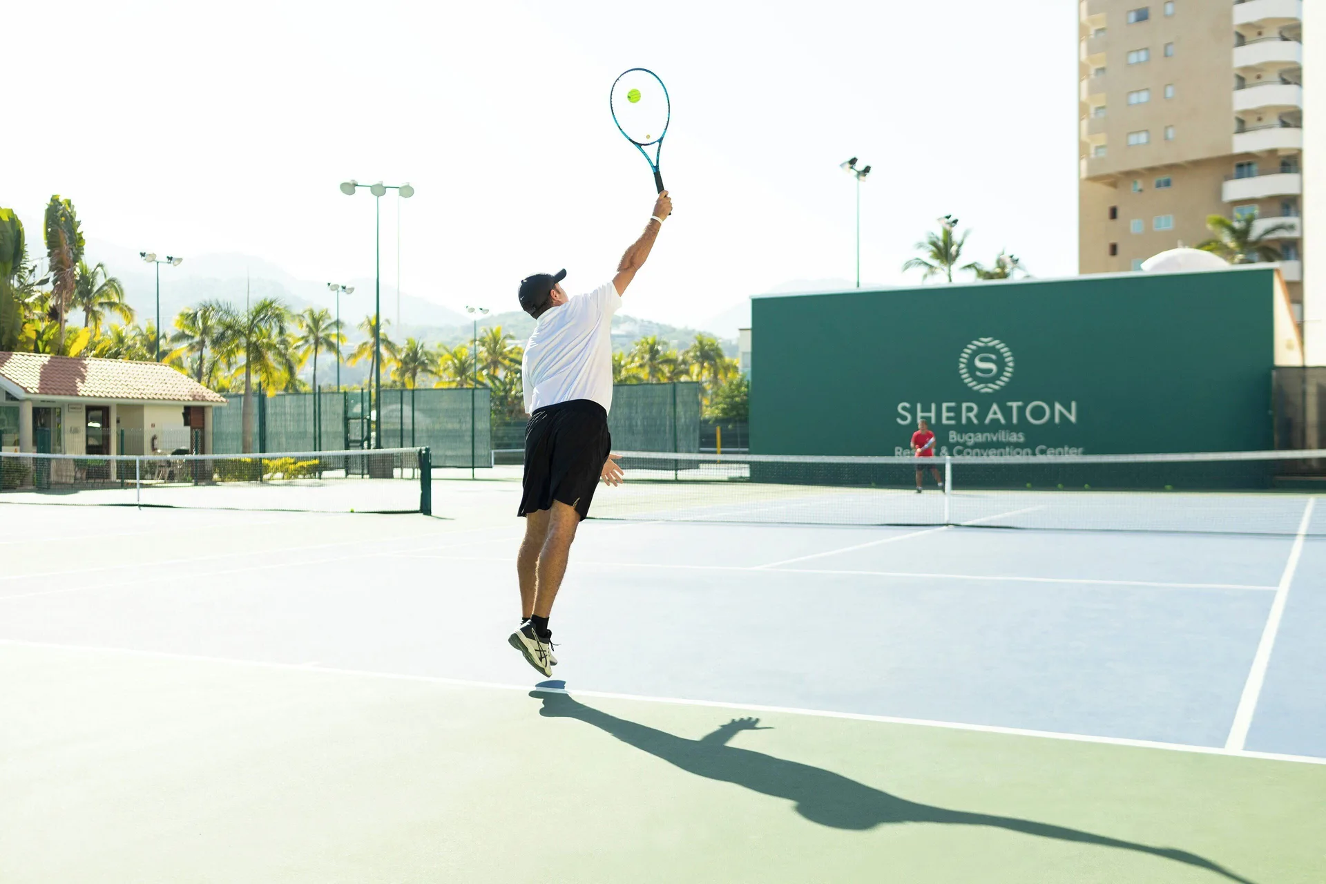 A tennis player serves on the resort court at Sheraton Buganvilias Puerto Vallarta.