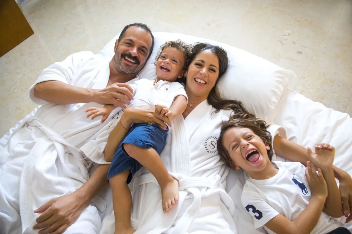 Family laughing together on a white bed at Sheraton Buganvilias Puerto Vallarta.