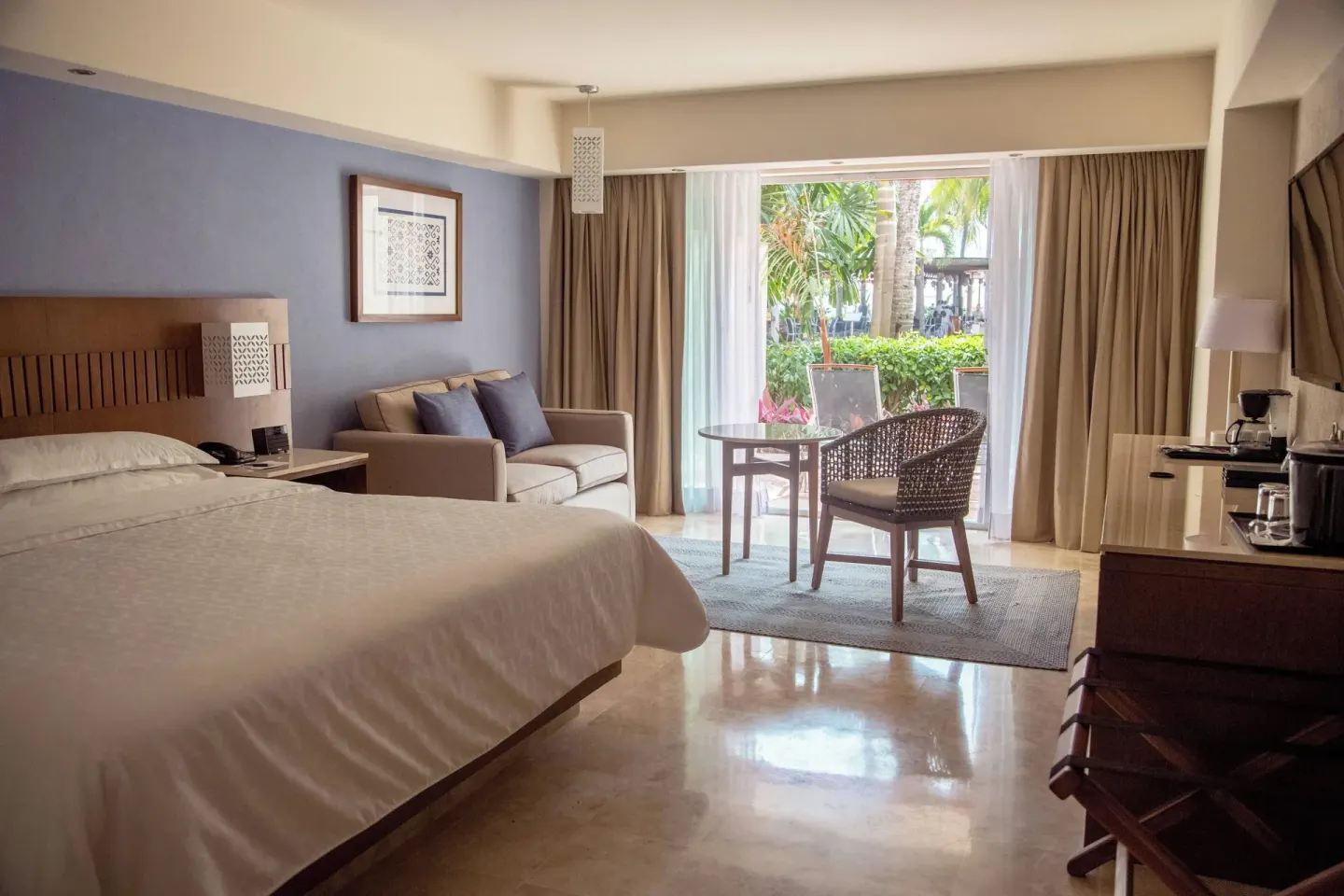 Deluxe room with king bed, sofa, seating area, and garden patio view at Sheraton Buganvilias Puerto Vallarta.