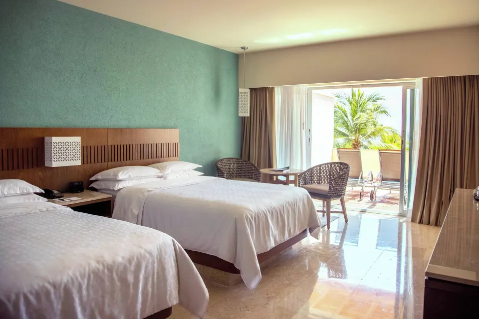 Deluxe room with two beds, seating, and open balcony doors at Sheraton Buganvilias Puerto Vallarta.