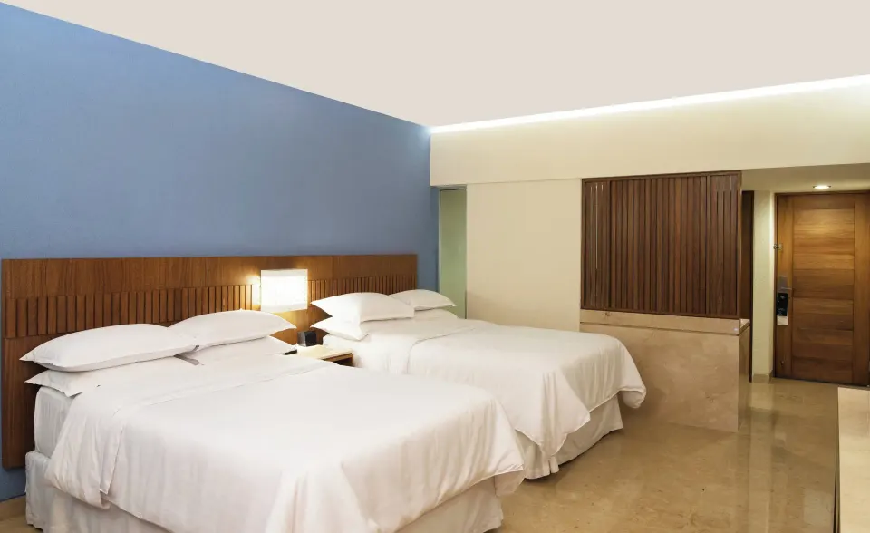 Deluxe room with two white beds and a blue accent wall at Sheraton Buganvilias Puerto Vallarta.