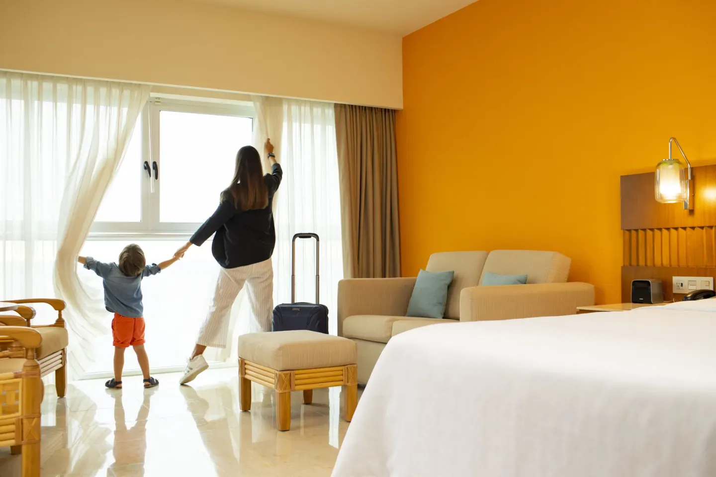 Deluxe room with white bed, orange wall, sofa, and bright window at Sheraton Buganvilias Puerto Vallarta.