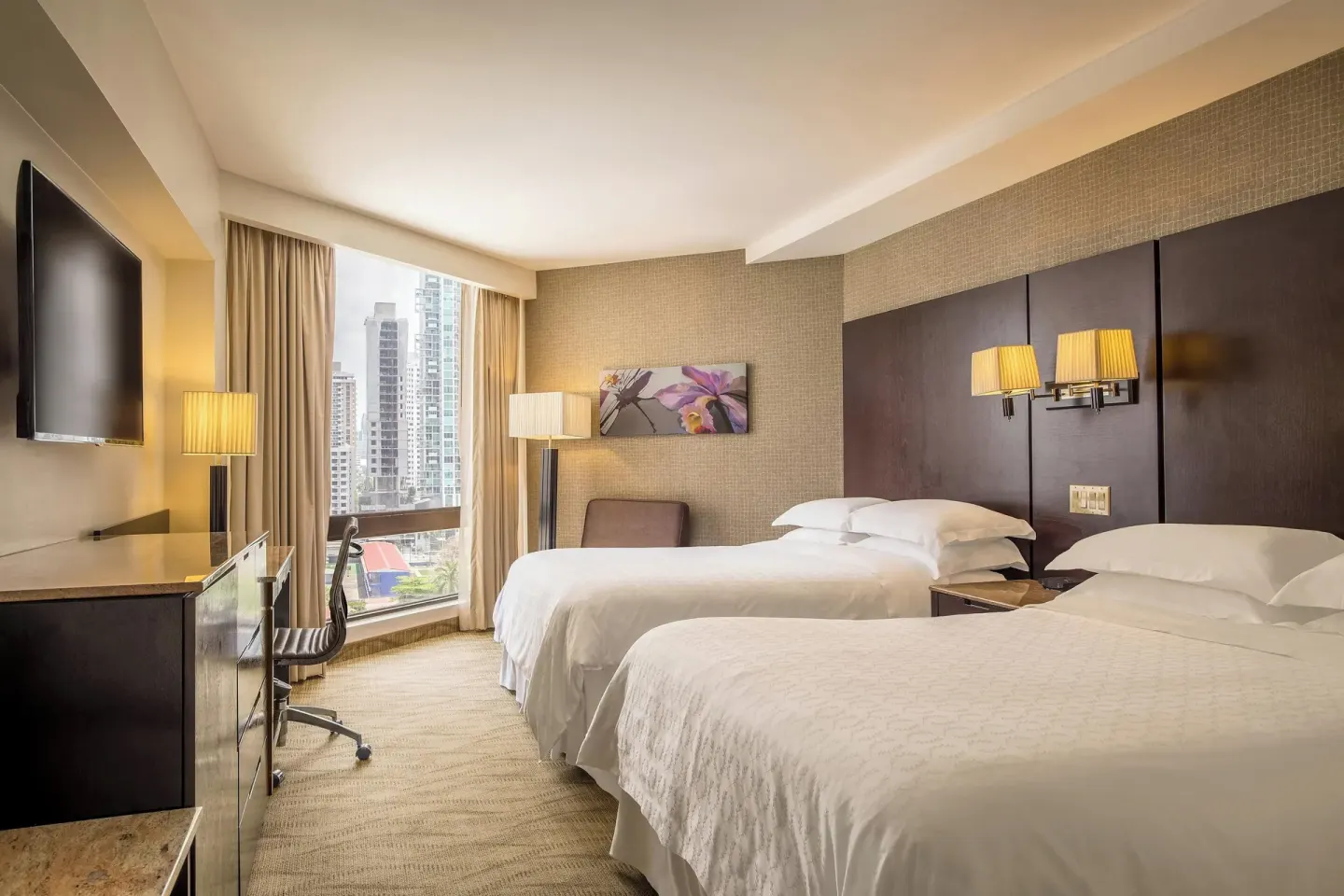 Deluxe Room with two beds, wall TV, desk, lamps, and city view at Sheraton Grand Panama.